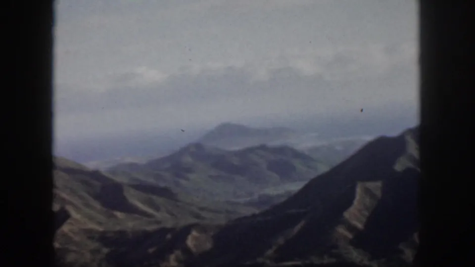 1959 Oahu home-movie view of layered mountain ridges and valleys beneath a pale, hazy sky.