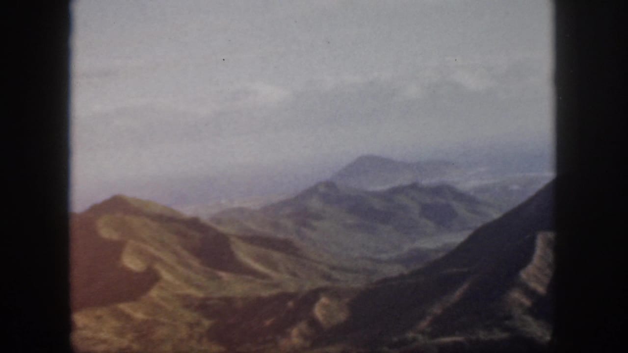 Warm-toned 1959 Oahu landscape frame showing ridges, shadowed slopes, and distant haze.