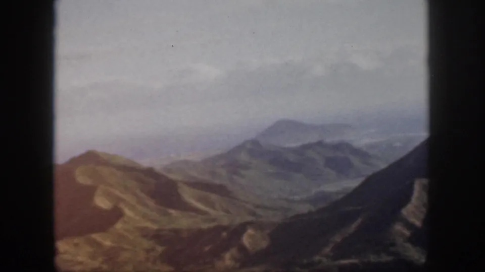 Warm-toned 1959 Oahu landscape frame showing ridges, shadowed slopes, and distant haze.
