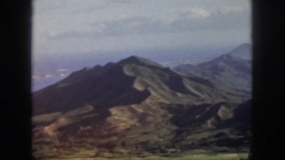 1959 Oahu home-movie frame showing dark foreground ridges, valley slopes, and distant hazy mountains.