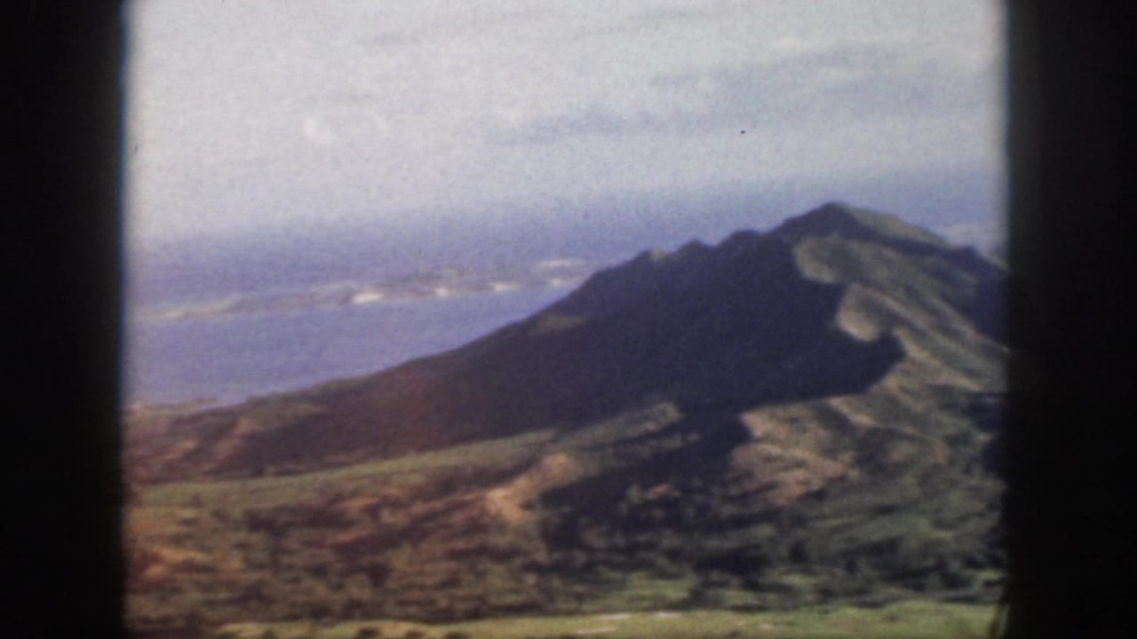 Mountain peak and green-brown slopes beside distant blue water.