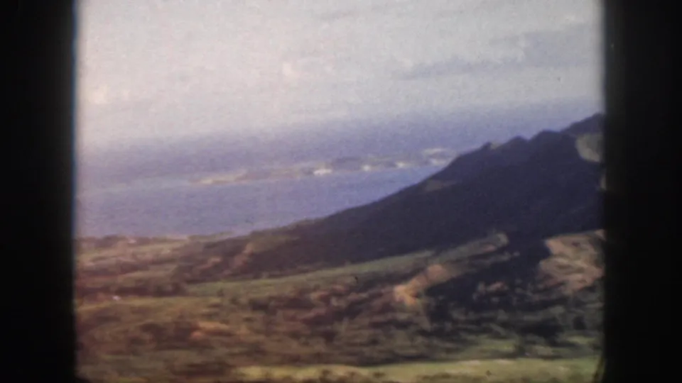 Oahu aerial home-movie view from 1959 showing coastline, low cloud, and a dark sloping mountain partly crossing the frame.