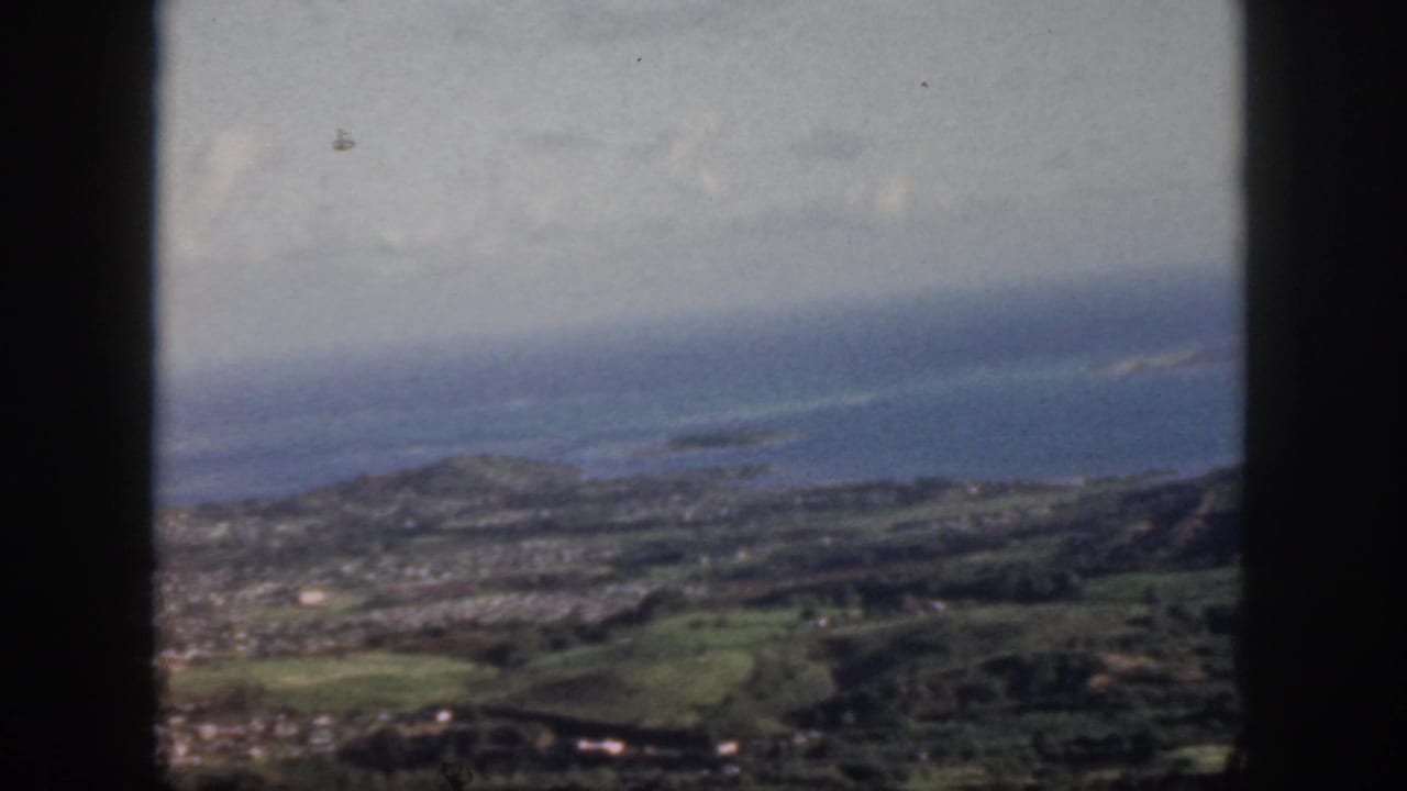 High aerial view of coastal terrain, ocean, roads or fields, and distant shoreline.