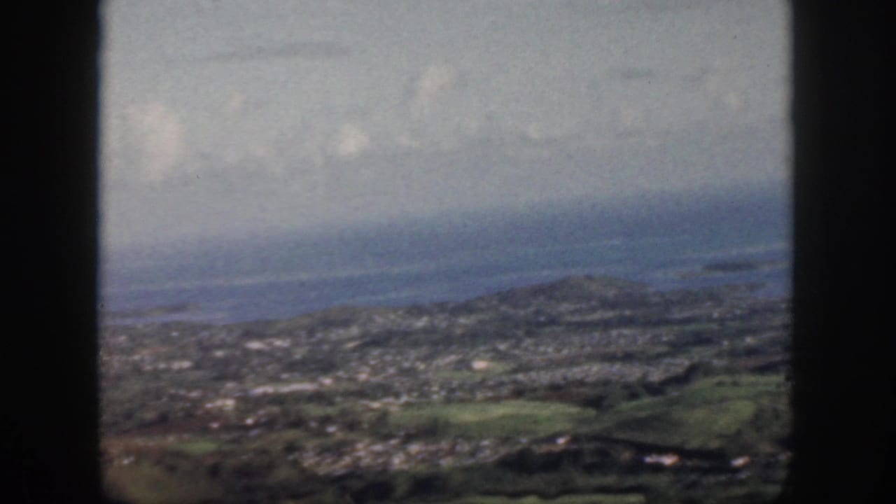 Coastal town, green slopes, and ocean horizon framed by dark vertical window bars.