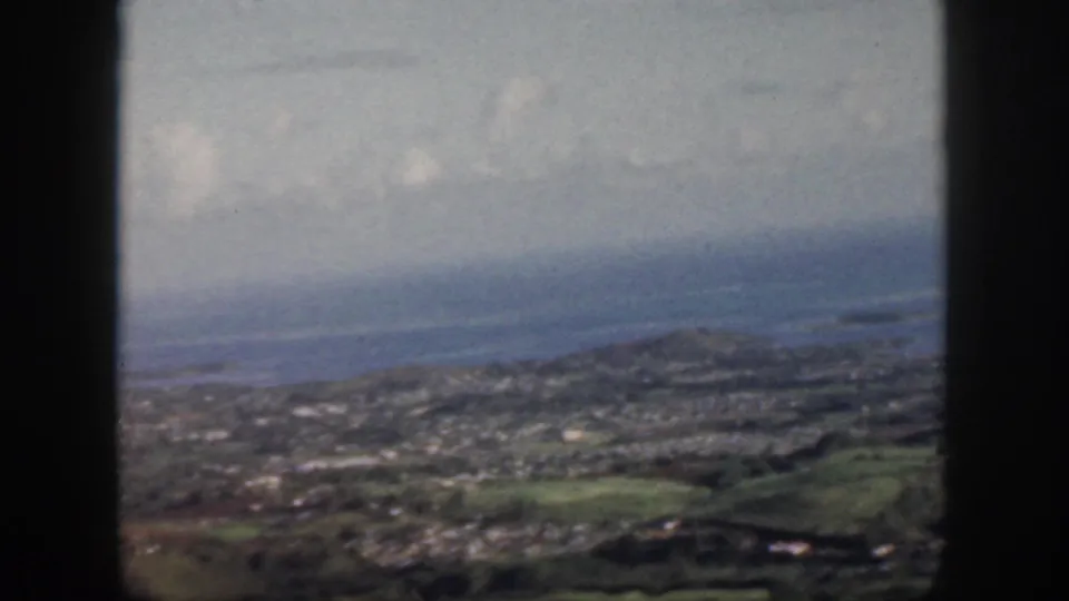1959 Oahu view across hillside neighborhoods toward the ocean, with dark window framing dividing the scene.