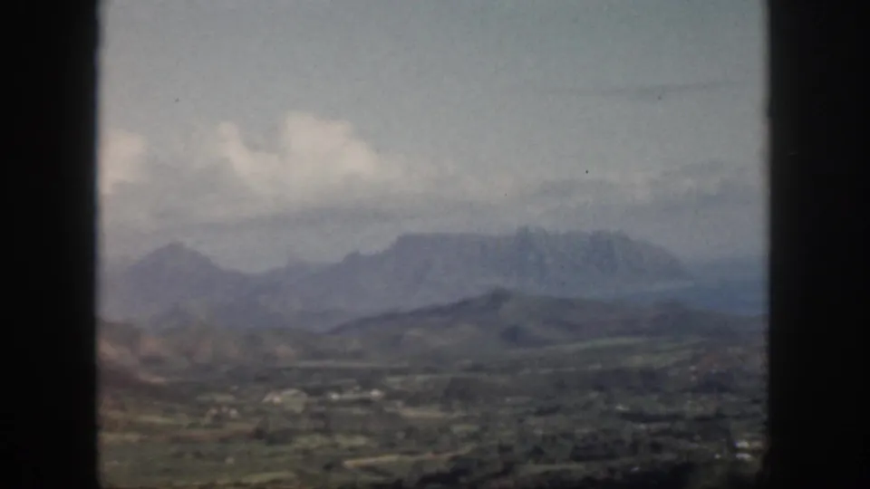 1959 Oahu 8mm frame showing a distant mountain ridge, green lowlands, clouds, and dark window framing.