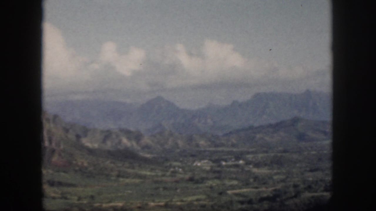 1959 Oahu scenic view through a window, with layered mountains, valley greenery, and pale clouds across the sky.