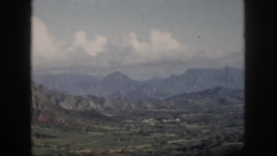 1959 Oahu scenic view through a window, with layered mountains, valley greenery, and pale clouds across the sky.