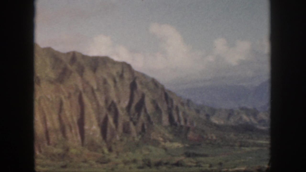 Rugged cliff face with vertical grooves above a green valley.
