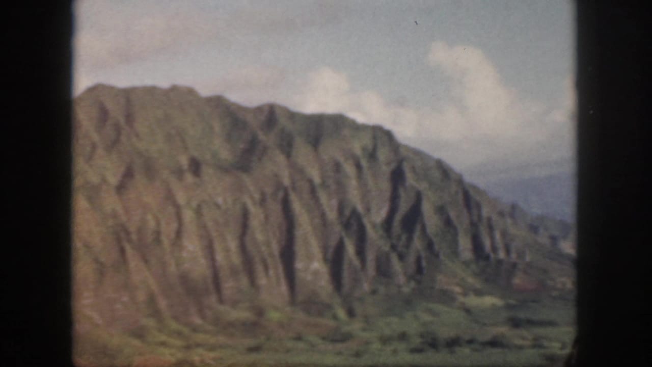 1959 Oahu 8mm frame showing a closer look at a steep ridged slope, valley vegetation, and a pale cloudy sky.