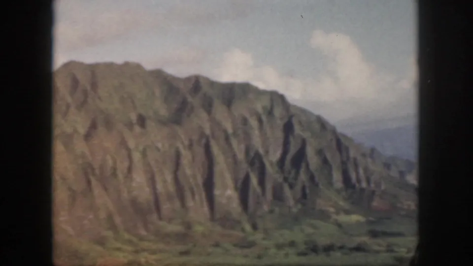 1959 Oahu 8mm frame showing a closer look at a steep ridged slope, valley vegetation, and a pale cloudy sky.