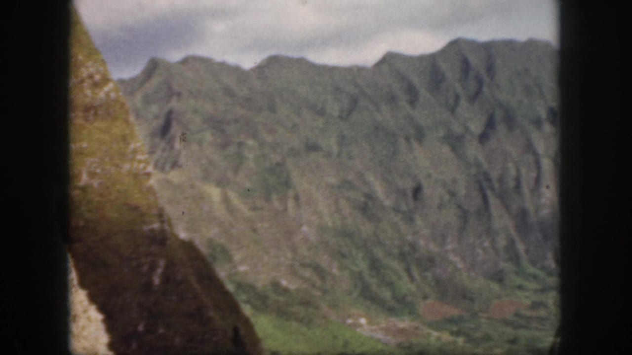 1959 Oahu landscape frame with a close sloping hillside at left and distant green mountains across the valley.