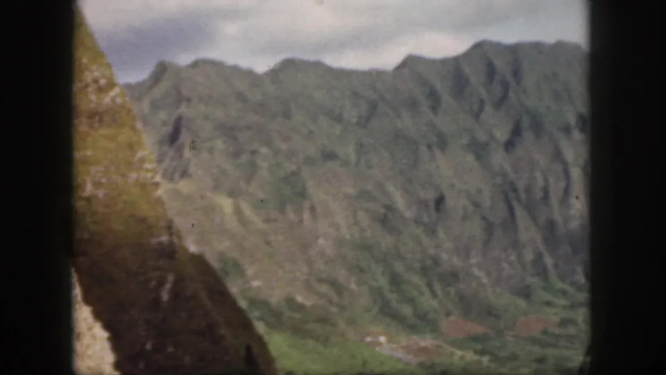 1959 Oahu landscape frame with a close sloping hillside at left and distant green mountains across the valley.