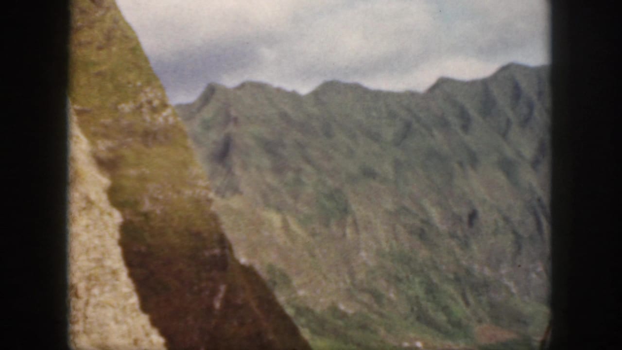 Oahu home-movie frame from 1959 showing a steep foreground hillside and receding green mountain ridges.