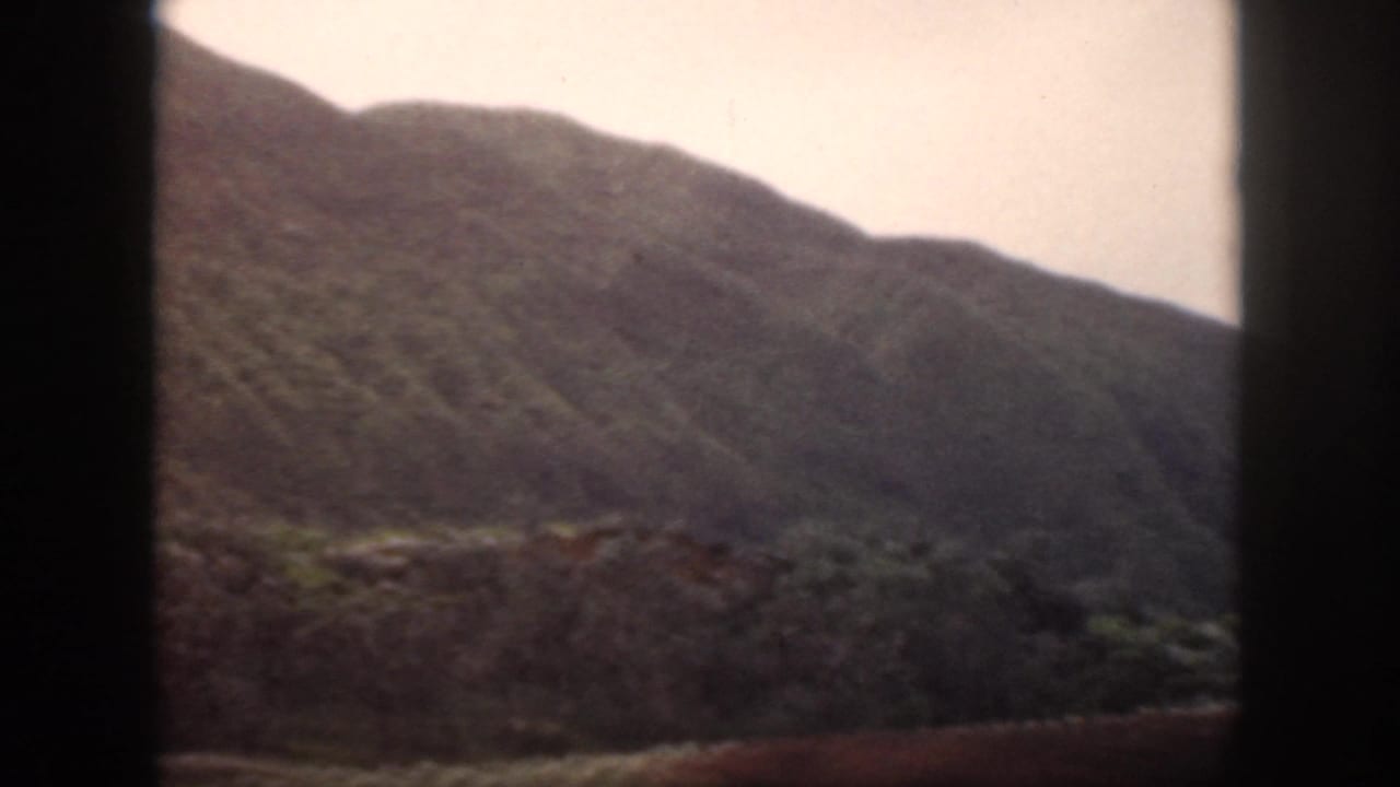 1959 Oahu 8mm frame showing a darker mountain ridge and hillside under a pale, overexposed sky.