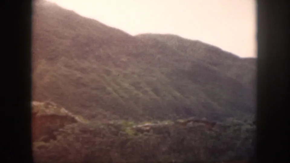 1959 Oahu 8mm frame showing a soft, distant mountain ridge with rocky foreground and pale daylight sky.