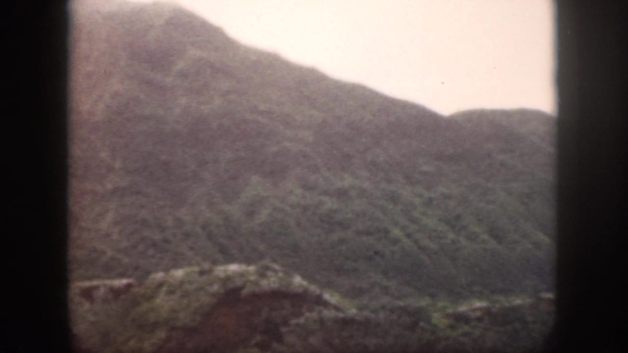 Rounded mountain slopes and rocky terrain beneath a bright pale sky.