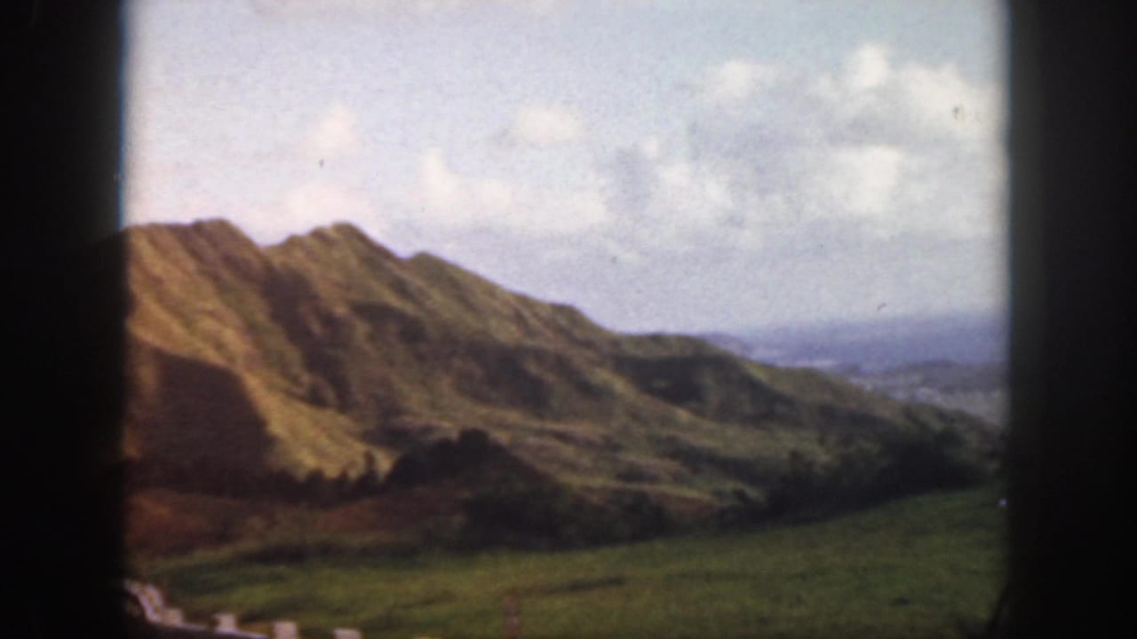 1959 Oahu 8mm view of a green mountain ridge dropping toward a broad valley under a partly cloudy sky.
