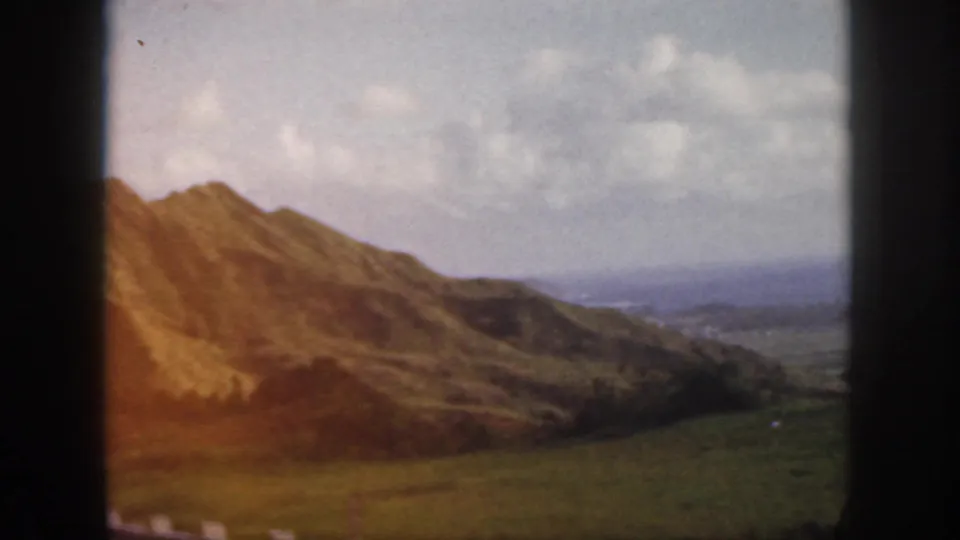 1959 Oahu 8mm frame showing a rugged ridge, green valley floor, and distant coastline or water through soft home-movie focus.