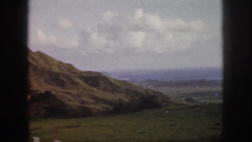 1959 Oahu 8mm closing frame with a sloped ridge, open valley, and hazy coastline under scattered clouds.