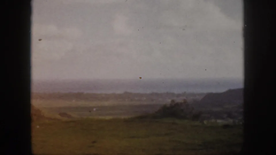 1959 Oahu home-movie view across open coastal grassland toward a hazy ocean horizon, partly bordered by dark frame edges.