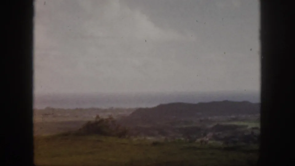 1959 Oahu 8mm frame with low hills, brushy vegetation, a distant ocean line, and pale cloud cover.