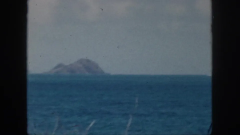 1959 Oahu coastal frame showing blue ocean, a prominent offshore island, pale sky, and soft 8mm color.