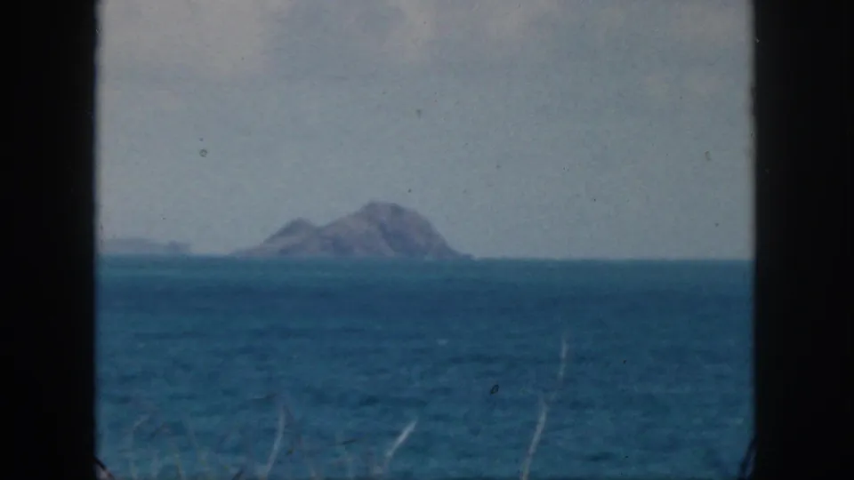 1959 Oahu 8mm frame showing a distant rocky islet beyond blue ocean with pale sky and dark film borders.