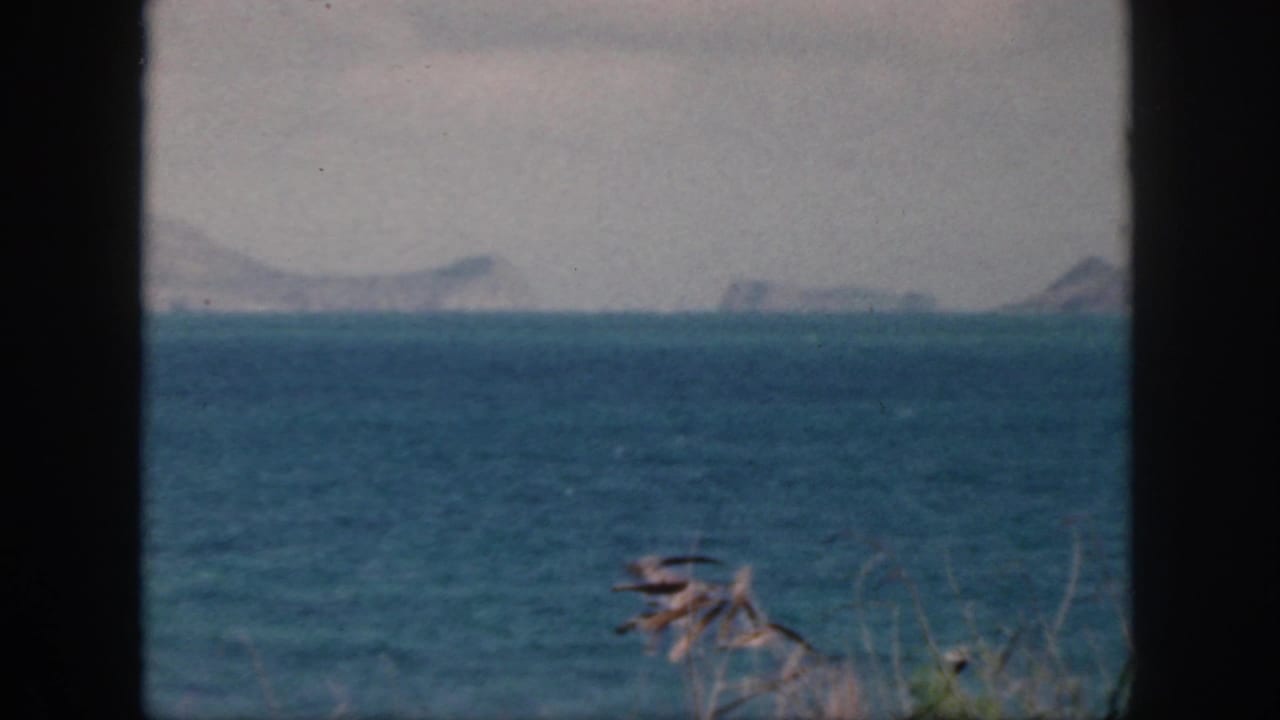 1959 Oahu home-movie view of blue sea and distant hazy mountains, seen through a dark window or doorway frame.