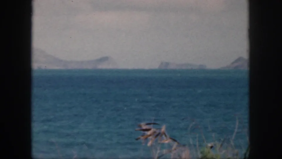 1959 Oahu home-movie view of blue sea and distant hazy mountains, seen through a dark window or doorway frame.