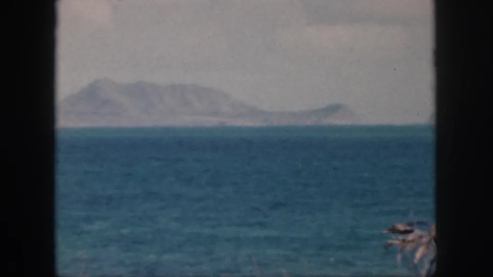 1959 Oahu 8mm frame looking across the sea toward hazy landforms, with soft color and visible film texture.