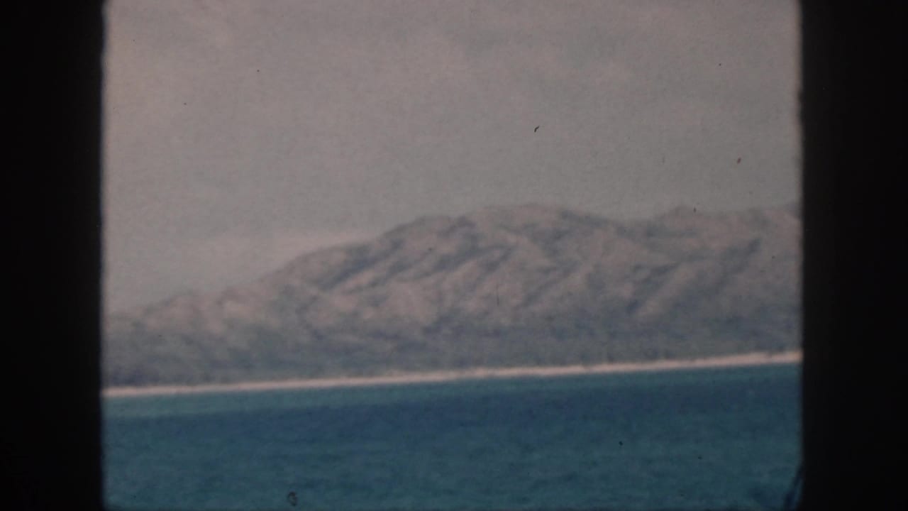 Mountainous island coast and narrow pale shoreline seen beyond the water through dark framing.