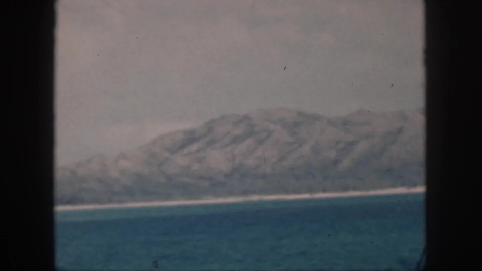 Oahu-area shore in 1959, with a rugged mountain ridge, pale surf line, and ocean viewed through a dark window-like frame.