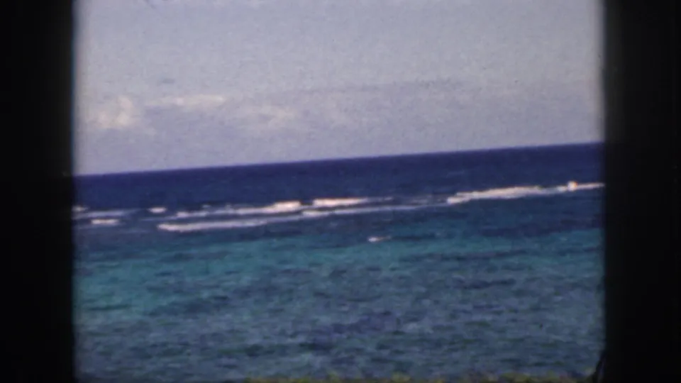 1959 Oahu coastal view focused on reef surf, turquoise water, a hazy horizon, and dark window framing.