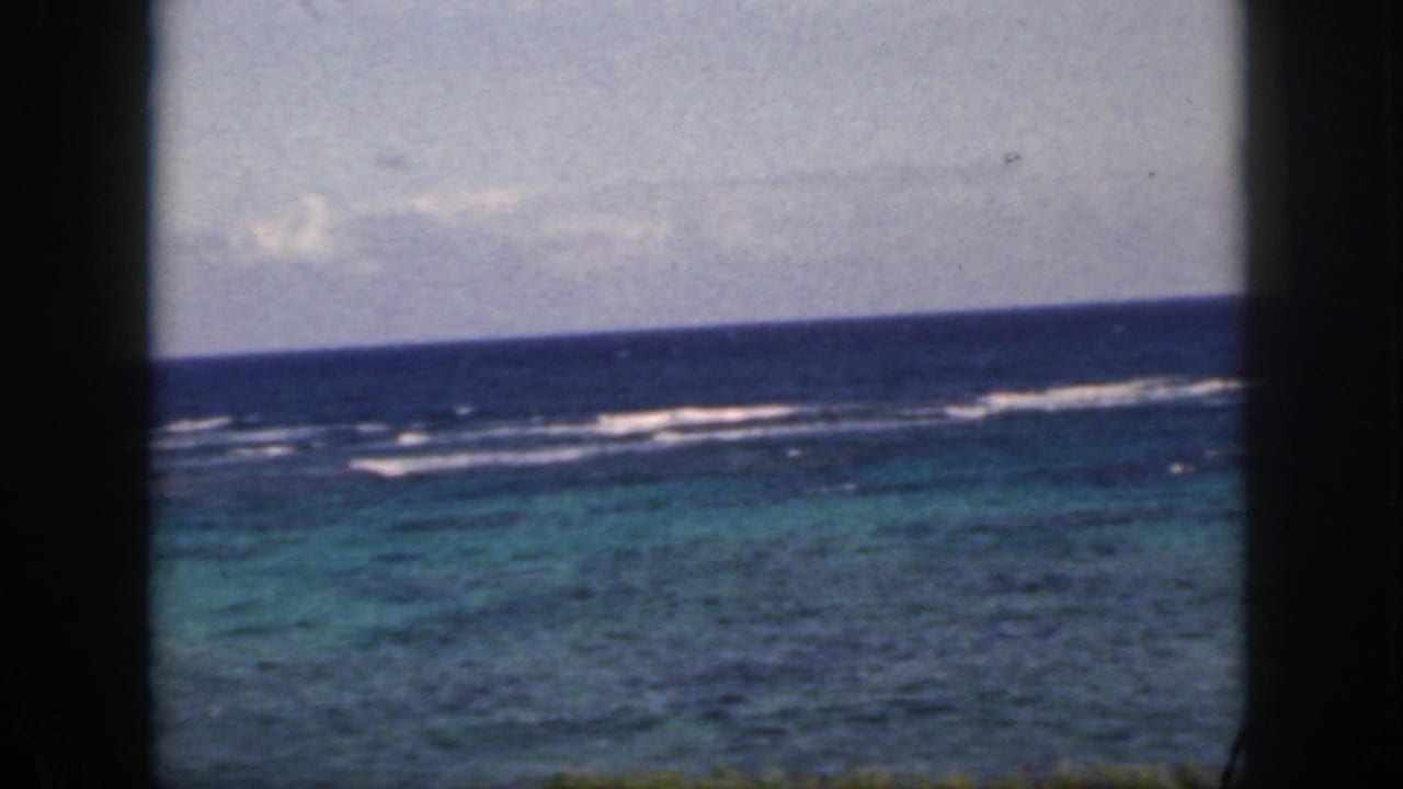 1959 Oahu home-movie frame showing turquoise and deep blue water, white surf, and cloudy sky viewed through dark vertical divisions.