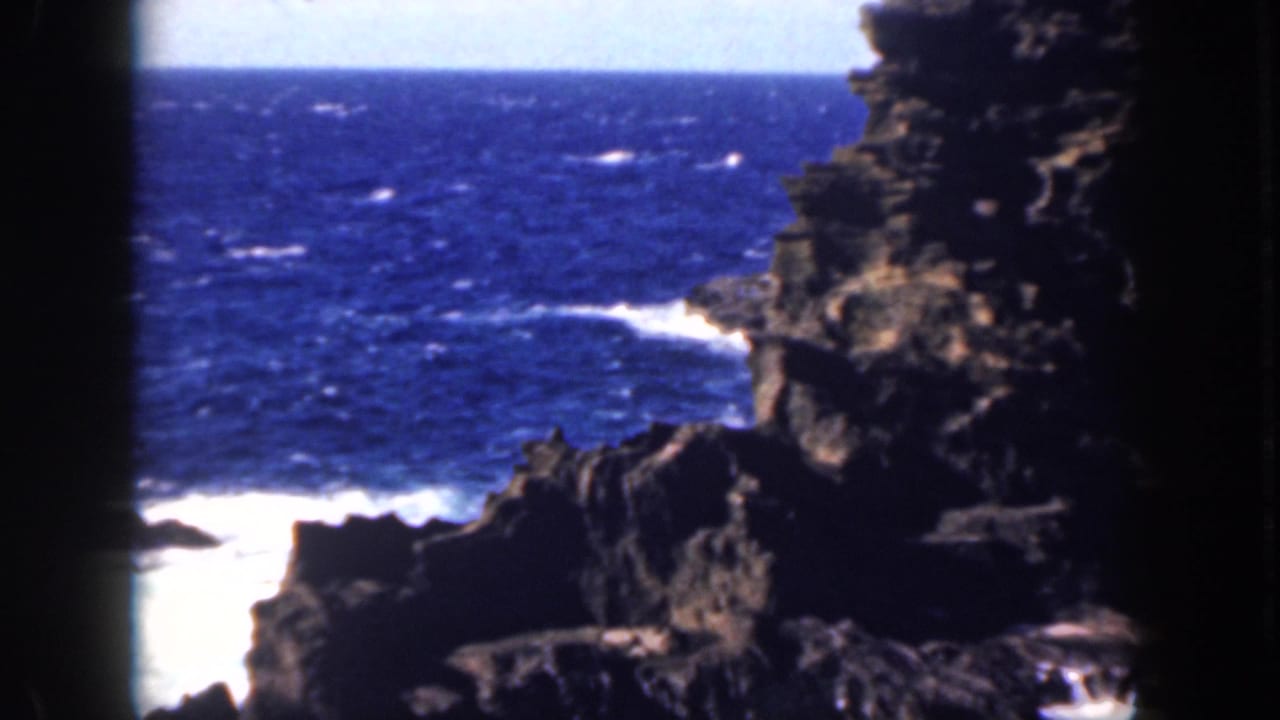 Rocky coastline at right with blue ocean and white waves below.