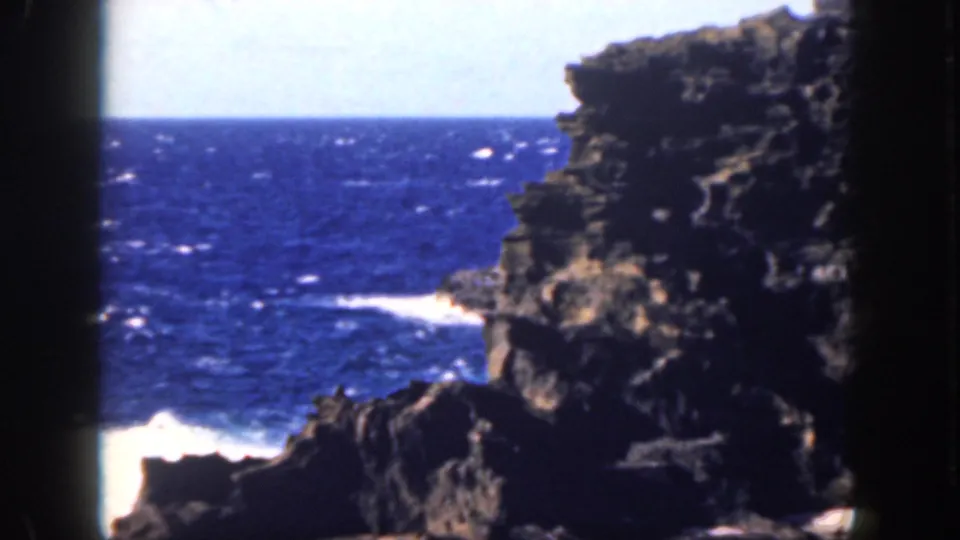1959 Oahu 8mm frame showing dark coastal rock, open blue water, white surf, and visible home-movie frame borders.