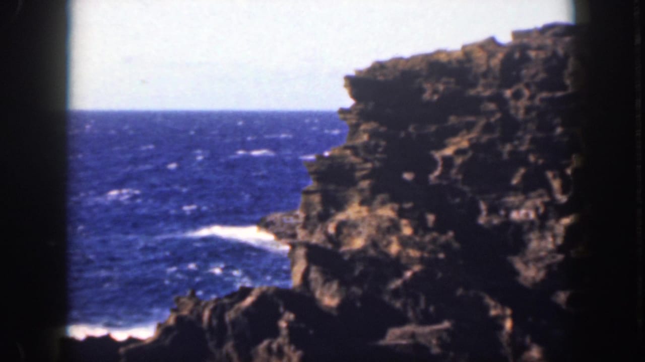 Rugged cliff edge above blue water with white surf along the shoreline.