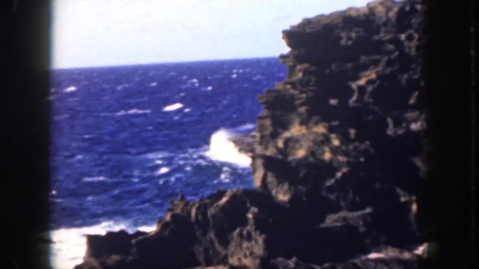Oahu 1959 home-movie view of white waves striking dark volcanic-looking rock beneath a bright ocean horizon.
