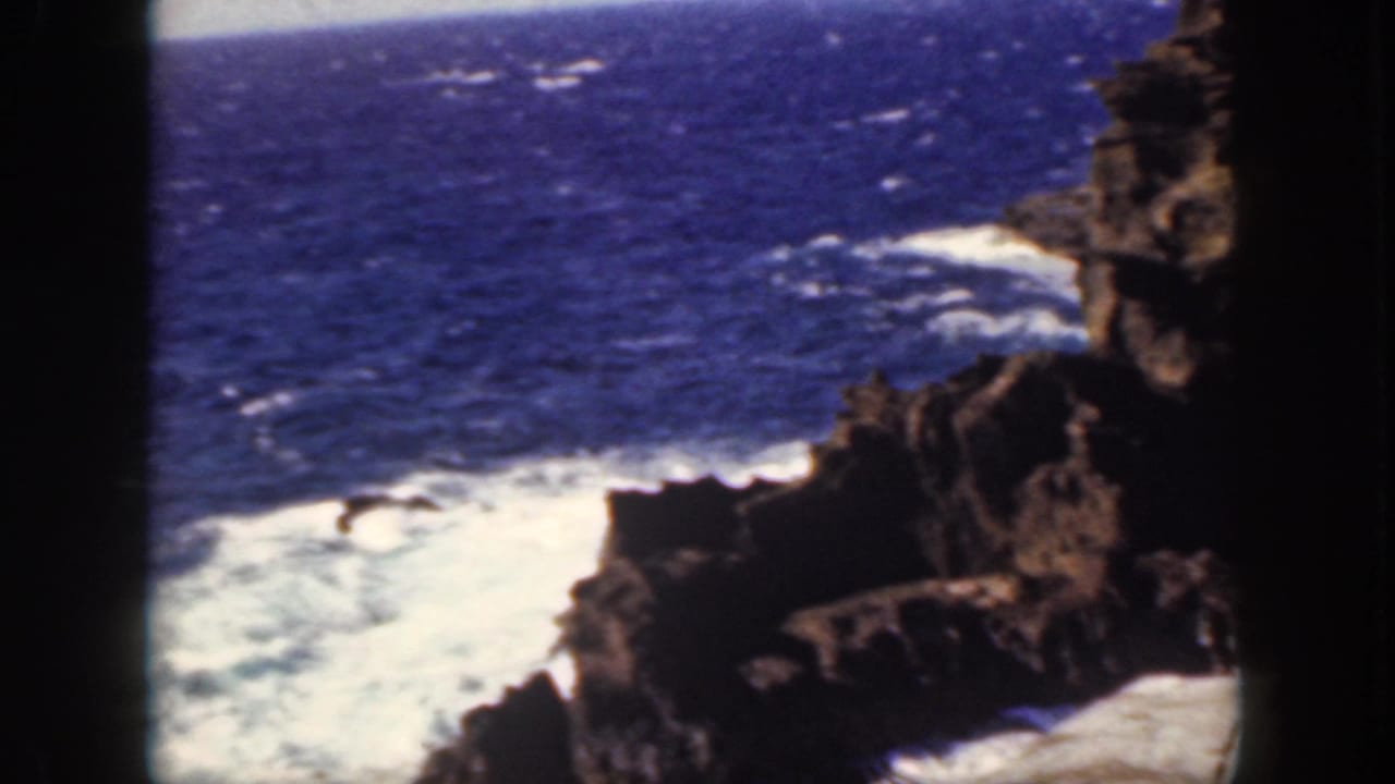 White surf churns around jagged coastal rocks beside a deep blue ocean.