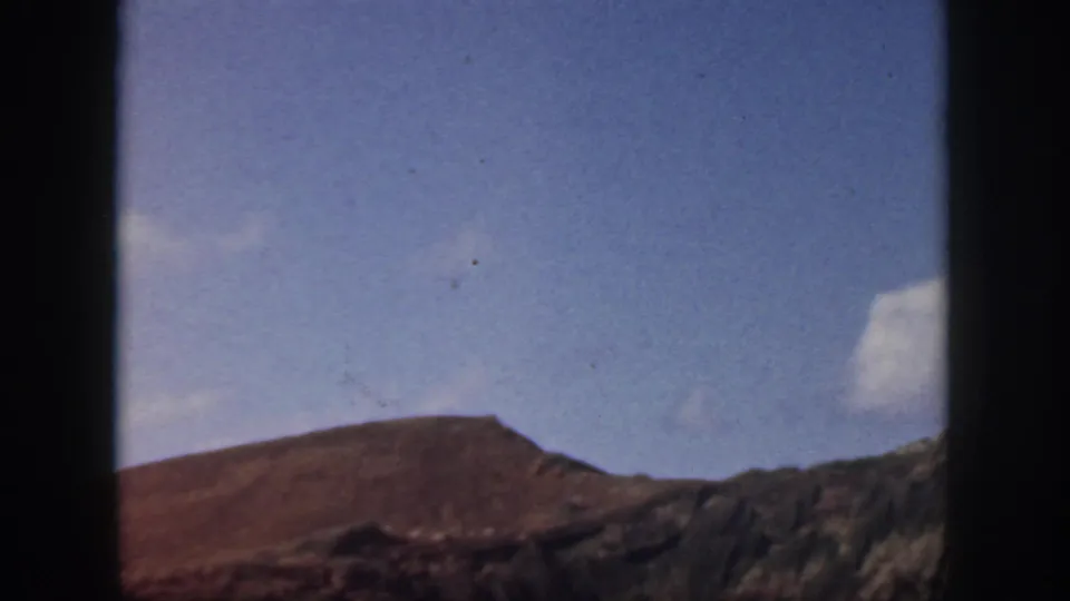 1959 Oahu home-movie frame shifting from shoreline to a mountain slope under clear blue sky.