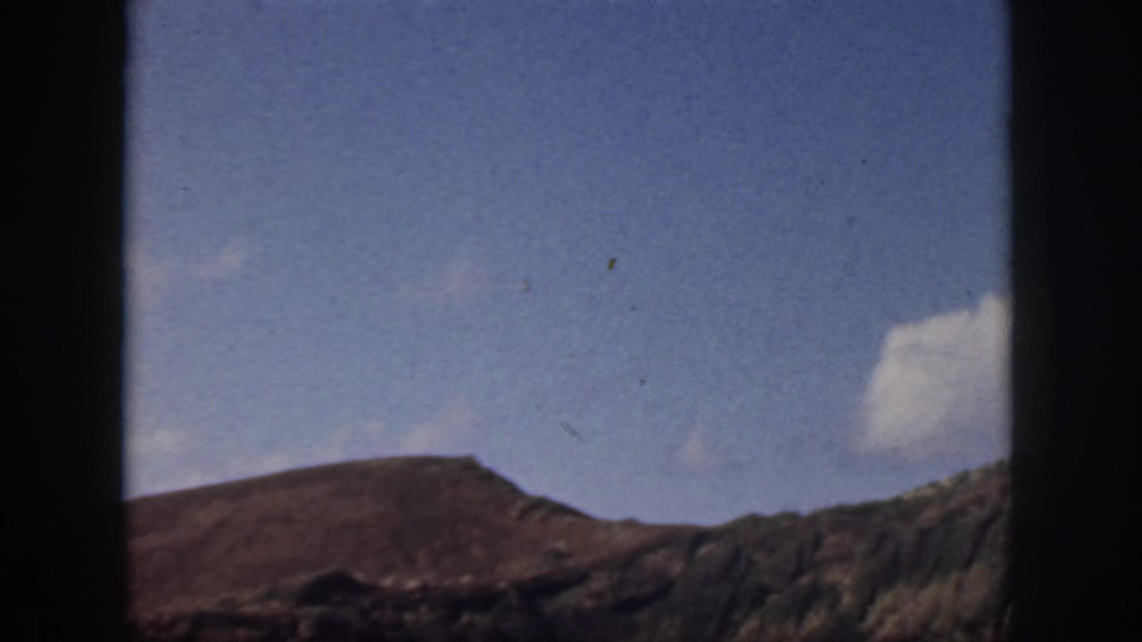 1959 Oahu landscape view with a low brown ridge, darker rocky slope, blue sky, and a bright cloud near the edge of frame.