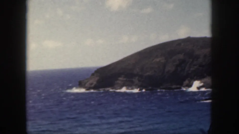 1959 Oahu 8mm frame of choppy ocean water and white surf against a dark rocky shoreline.
