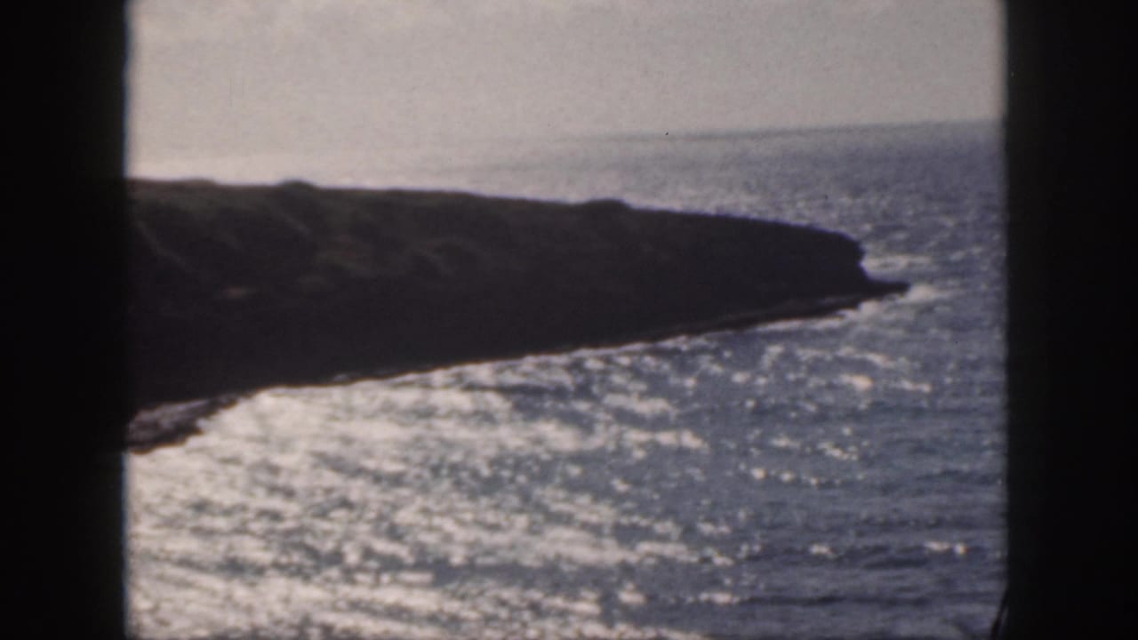 Rocky shoreline and sunlit ocean waves seen through dark 8mm film borders.