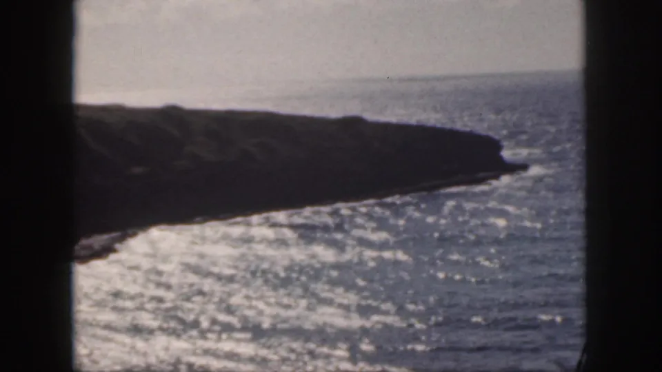 1959 Oahu 8mm frame showing a rocky point, bright surf, and open ocean viewed from the shore.