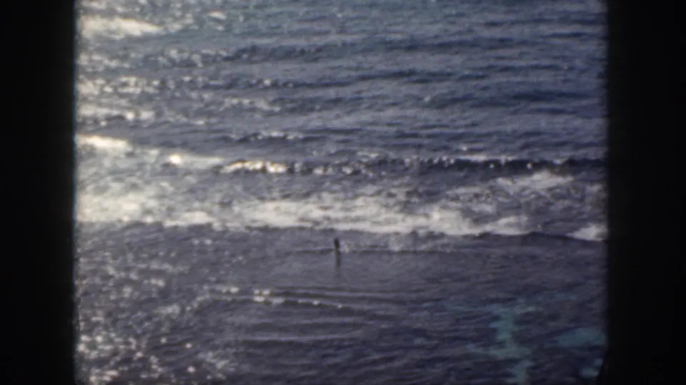 1959 Oahu 8mm frame showing a lone figure in the surf beneath a sunlit ocean surface.