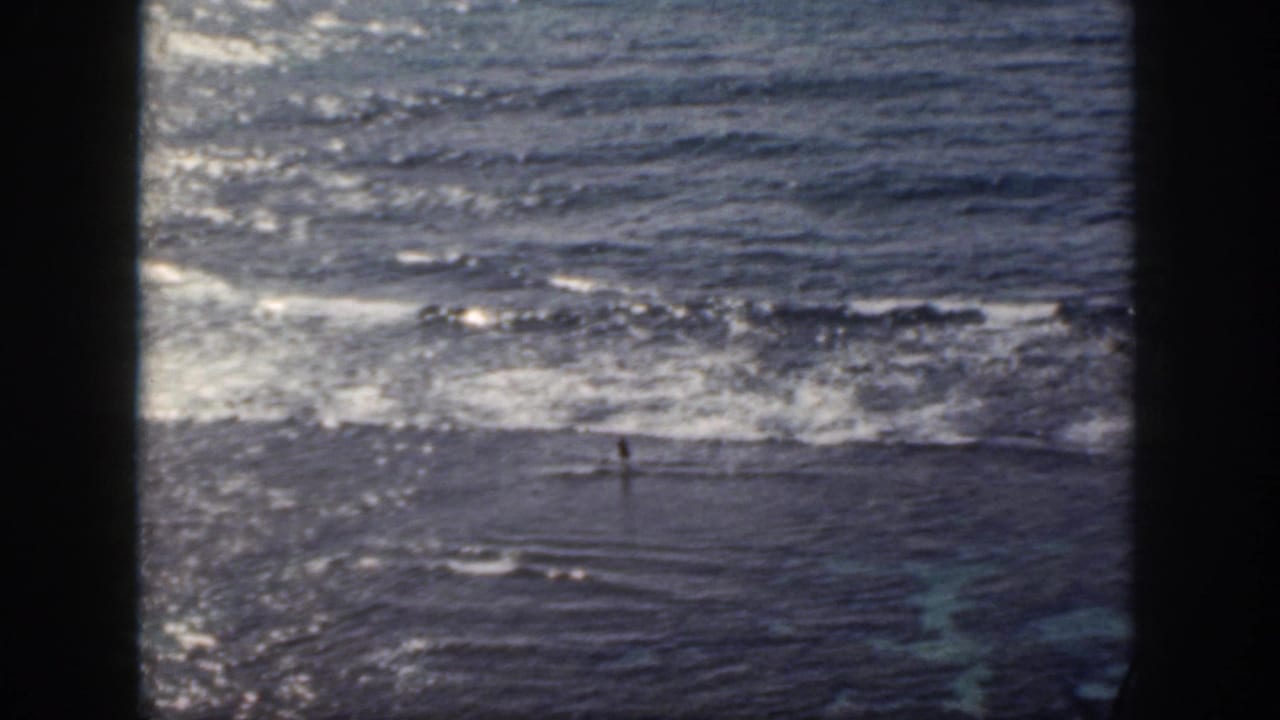 1959 Oahu 8mm frame showing a distant swimmer in choppy water as waves break across the upper part of the view.