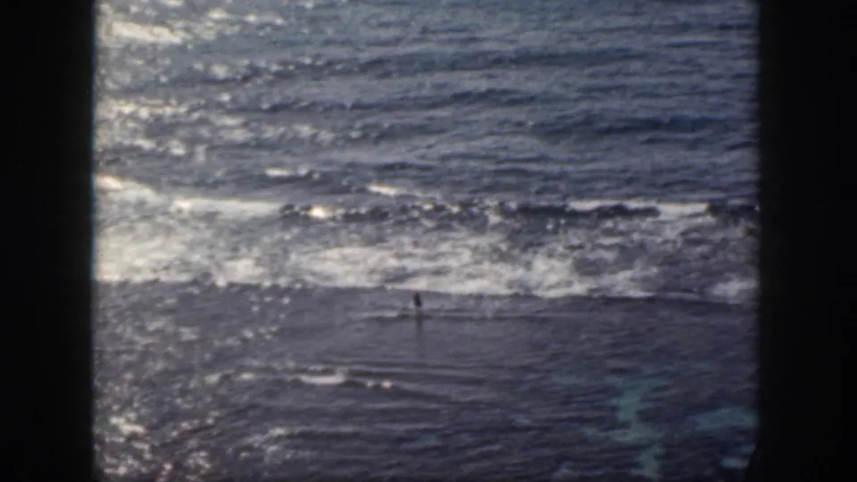1959 Oahu 8mm frame showing a distant swimmer in choppy water as waves break across the upper part of the view.