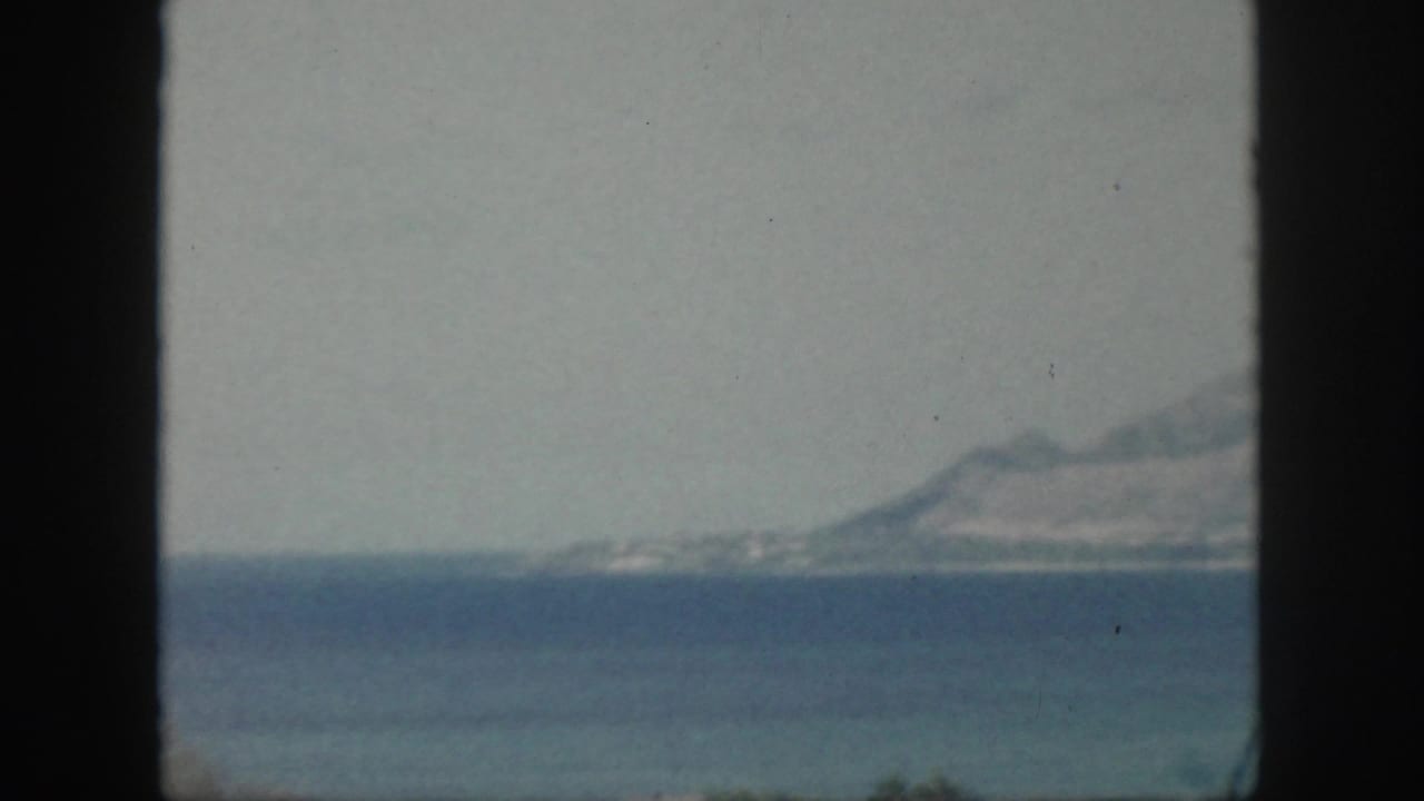 Distant coastline and mountains across blue water, divided by a dark vertical frame.