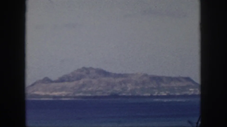 Final 1959 Oahu frame showing the distant mountainous island and shoreline across the sea with soft 8mm color.